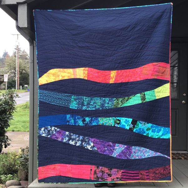 front view of quilt. background is dark blue and there are thick rivers of rainbow colored fabrics in the bottom two thirds of the quilt. edging is a similar rainbow of fabric.