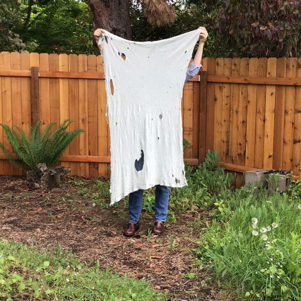 woman stands outside holding a large baby blanket that stretched 5 feet. It is well loved and covered in holes.