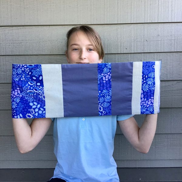 young girl holding up a scarf in blue tones, made from scraps of an old baby blanket and coordinating fabrics