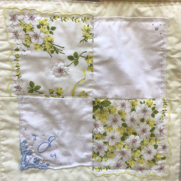 Image is a closeup of one quilt block composed of 4 vintage hankerchiefs on a cream background.