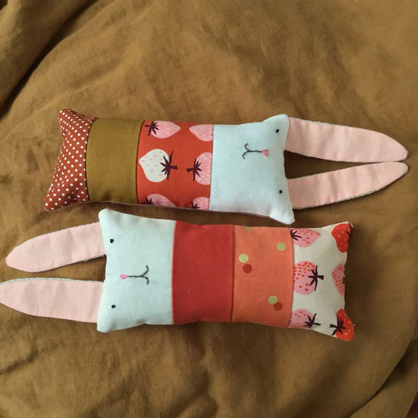 Image shows two patchwork bunnies next to each other. Both are in shades of pink, red and brown, with long pink ears and embroidered faces.