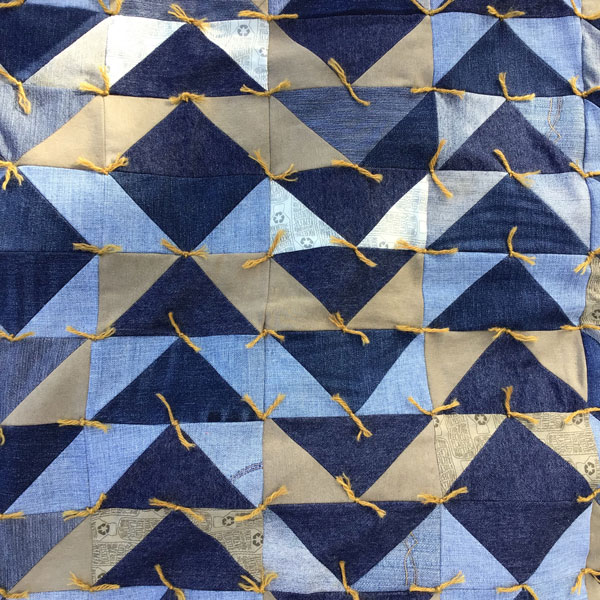 Image is a closeup of denim and khaki triangles tha make up the quilt, with ochre yellow ties.