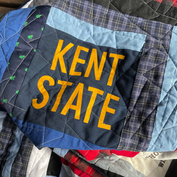 Close up a quilt square in shades of blue with "KENT STATE" in the center in yellow.