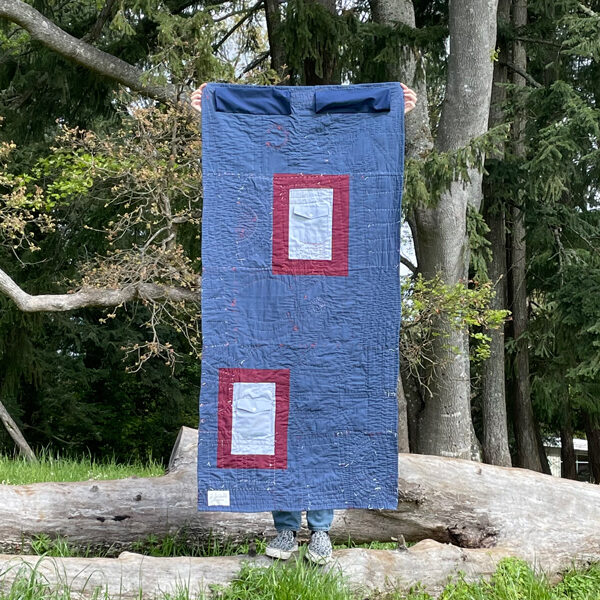 Back of long rectangular quilt. Background is dark blue. There are two light blue shirt pockets on the back, framed in maroon fabric.