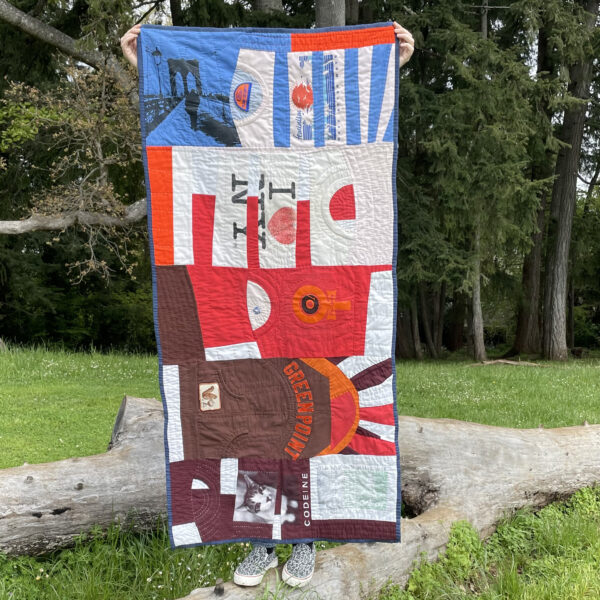 Long rectangular quilt composed of various deconstructed Tshirts in shades of light blue, pink, brown, maroon and red. Graphic themes include music, feminism and New York State and Brooklyn.